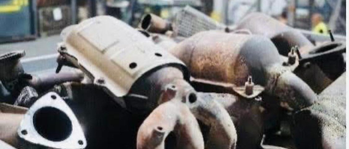 Spent catalytic converters and exhaust manifolds heaped in a collection bin at a dismantling yard