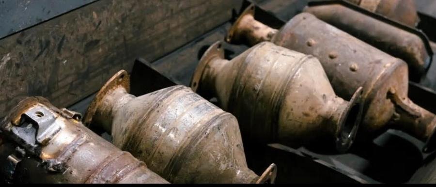 Decanned catalytic converter shells lined up along a processing bench