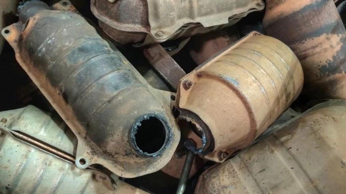 A heap of spent catalytic converters, shells scorched and flanges cut