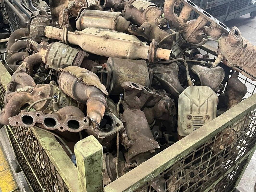 Spent catalytic converters and exhaust manifolds in a steel stillage cage at a dismantling facility