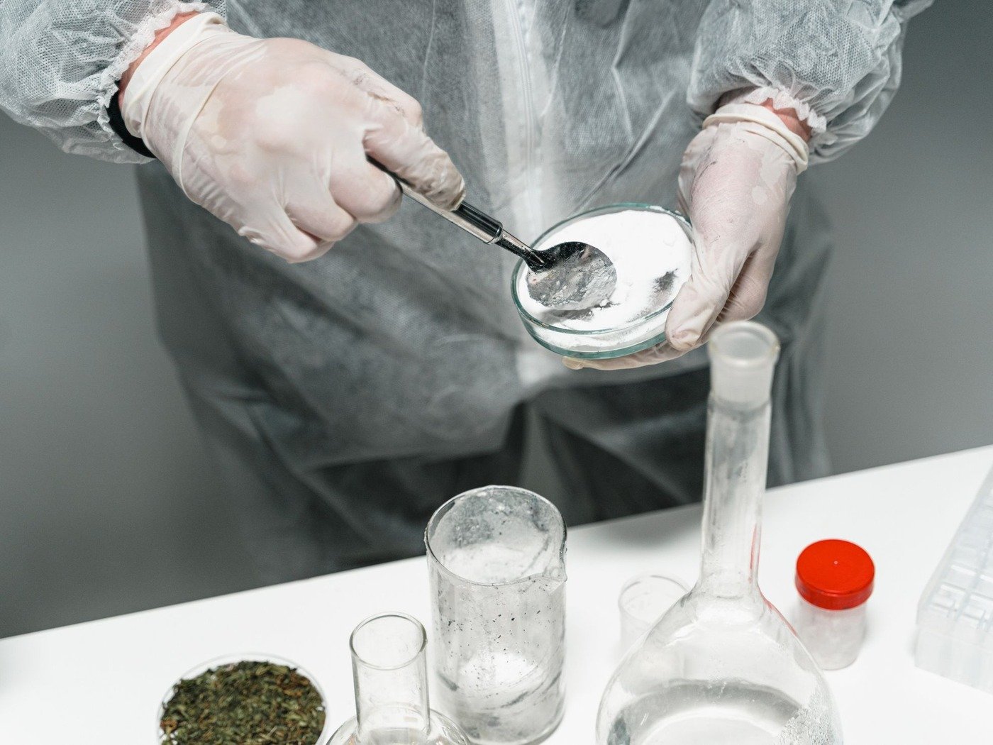 A gloved technician spooning a powder sample into a dish for analysis